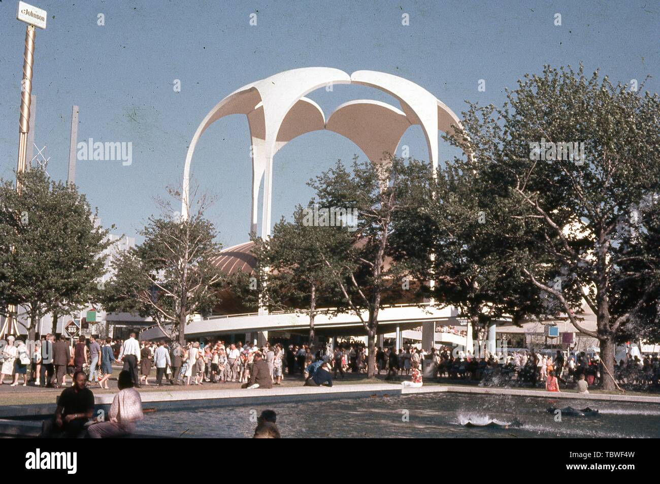 Messebesucher gehen und sitzen in der Nähe von einem Brunnen, an einem sonnigen Tag, vor der Johnson Wax Pavillon, 1964 in New York World's Fair, Flushing Meadows Park, Queens, New York, Juni, 1964. () Stockfoto