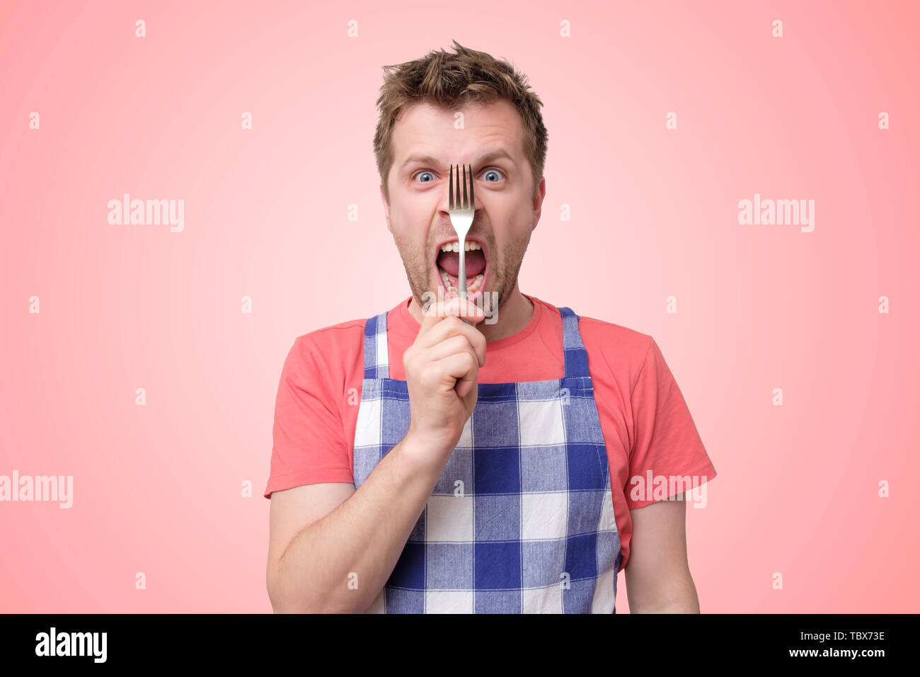 Mann in Schürze mit nervösen Krise auf rosa Hintergrund isoliert Stockfoto