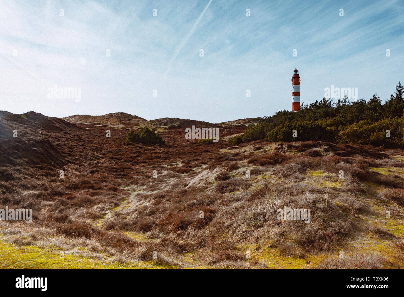 Malerische Landschaft mit roten Leuchtturm auf dem Hügel in der Ferne gegen bewölkten Himmel und trockenes Gras im Vordergrund. Idyllischer Blick aus niedrigen Winkel Stockfoto