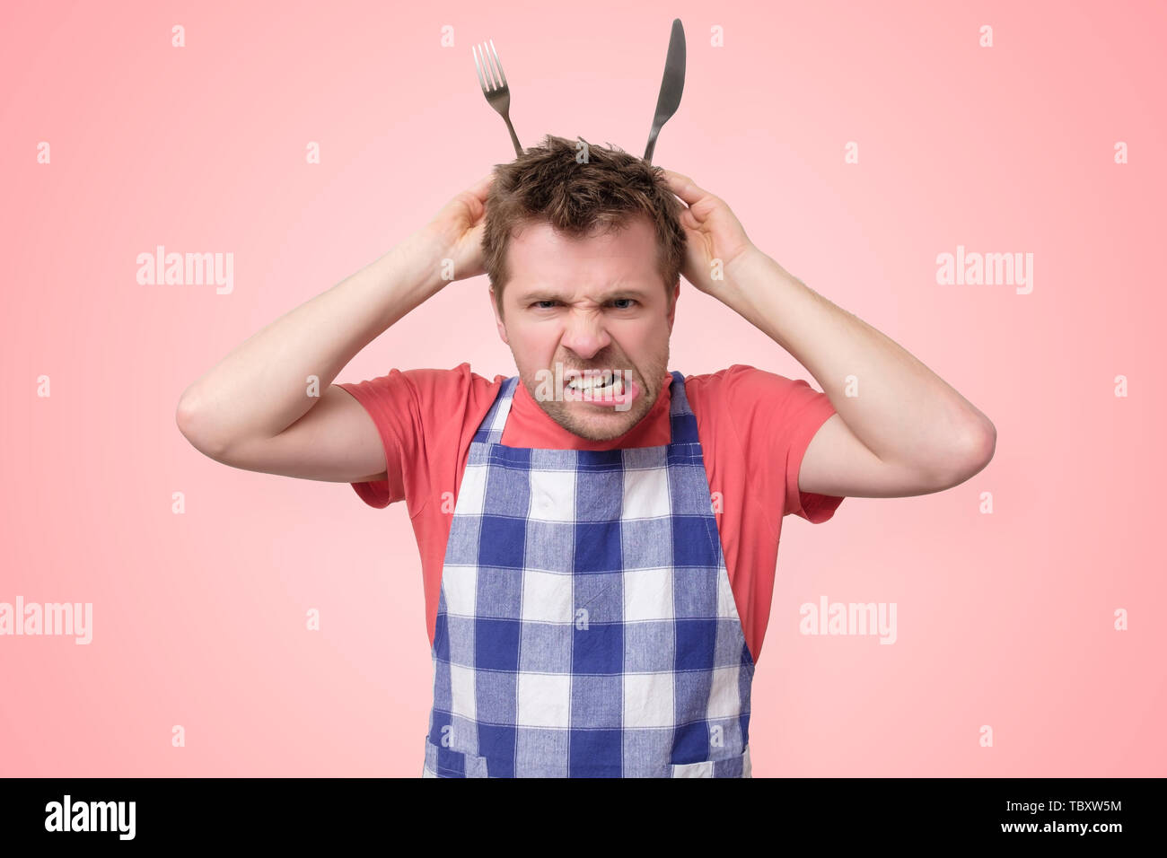 Mann in Schürze mit nervösen Krise auf rosa Hintergrund isoliert Stockfoto