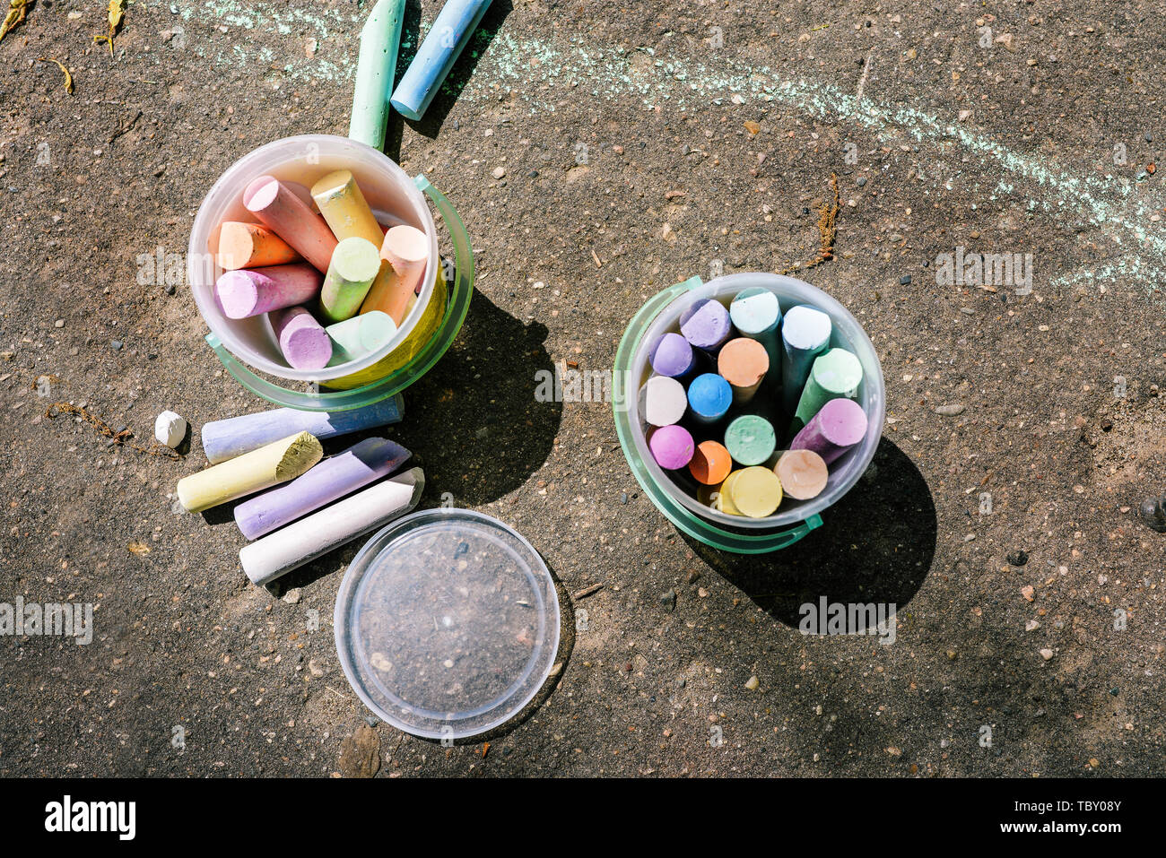 Kunststoffeimer mit Kreide zum Zeichnen auf Asphalt. Mehrfarbige Wachsmalstifte für Kinderzeichnungen. Zeichnen mit Kreide auf Asphalt. Spaß auf dem Spielplatz Stockfoto