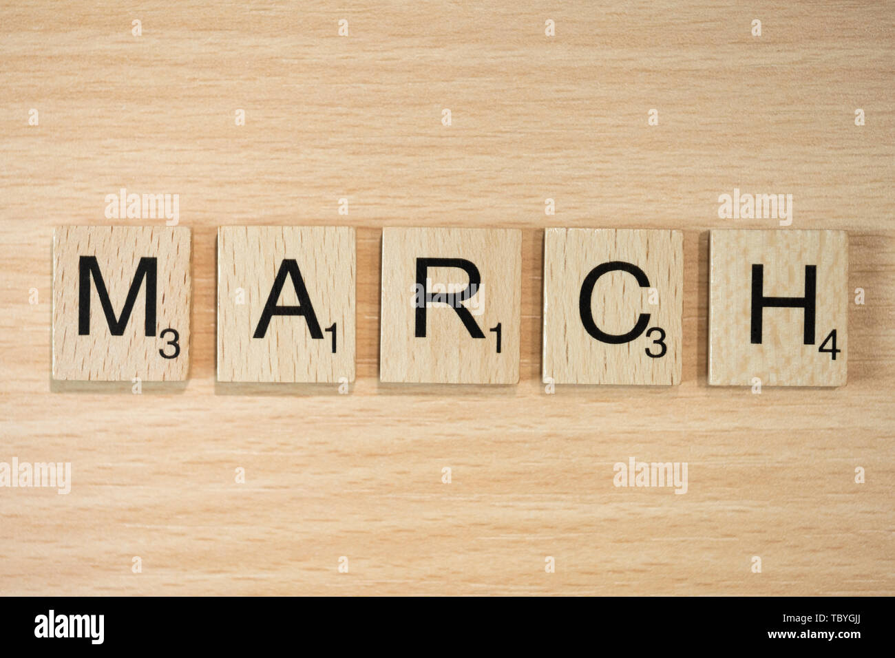 Das Wort März, Dinkel mit Holz Fliesen auf einem Holz Wirkung Hintergrund mit Scrabble nummeriert Punktzahl Werte. Stockfoto