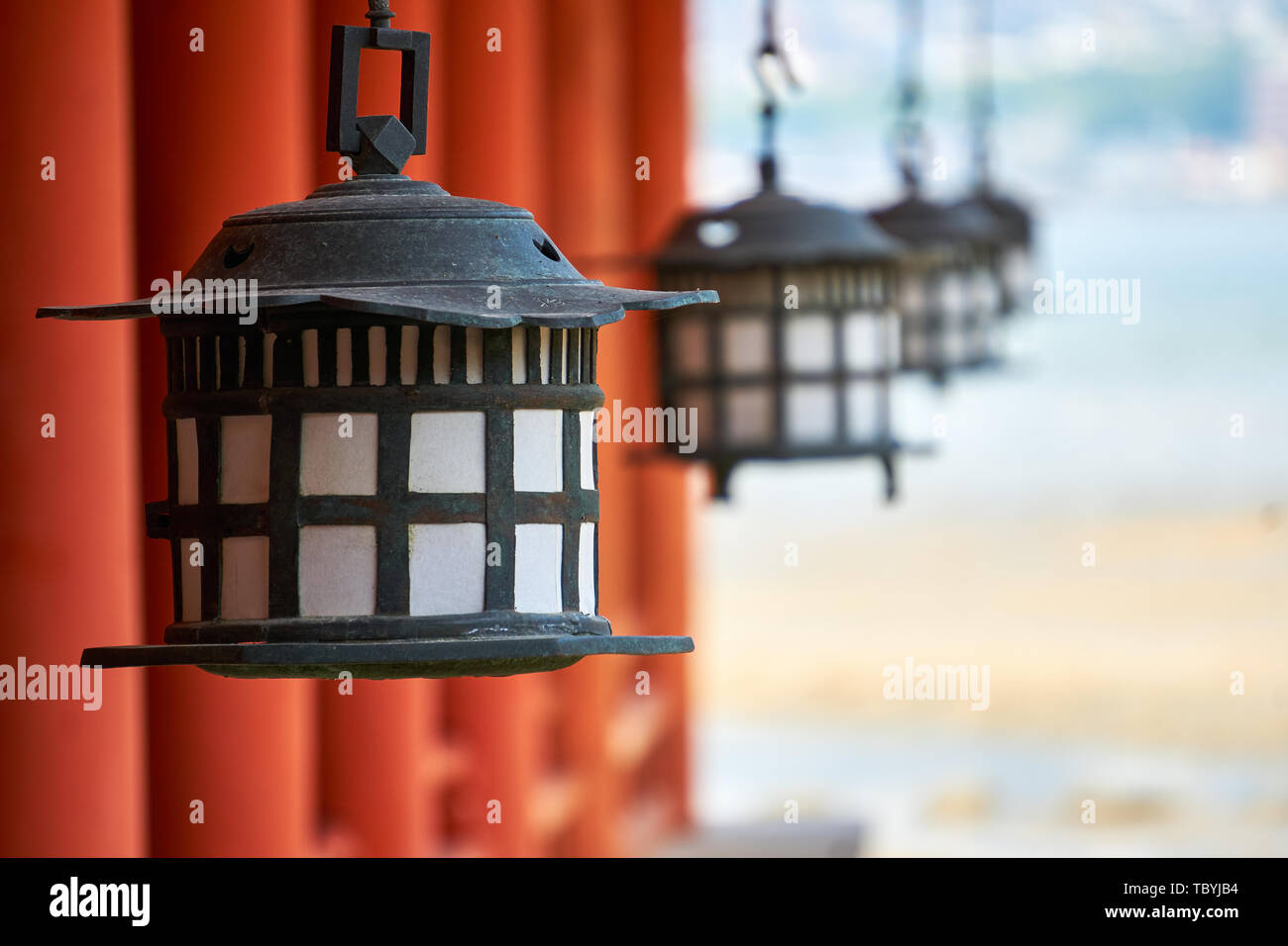 Schwarze und weiße Laternen hängen in einer Reihe von Spalten in Zinnoberrot Itsukushima Jinja Schrein in Miyajima, Japan, mit der Seto Inland Sea hinter sich. Stockfoto