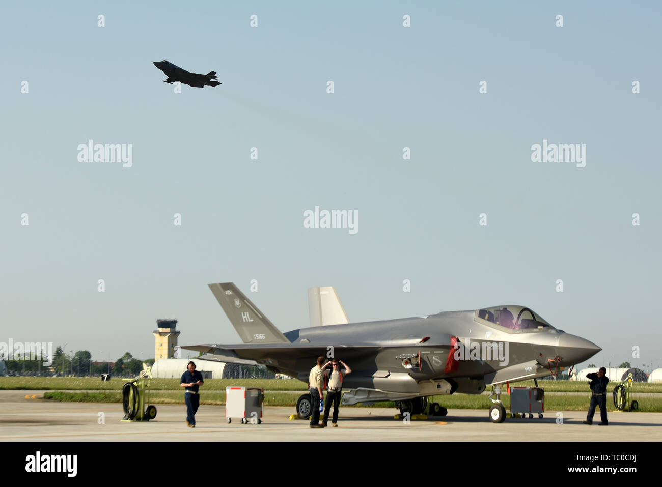 Eine F-35A Lightning II Kampfflugzeug sitzt auf der Flightline, während eine andere F-35 ein Weg nimmt während der ASTRALEN Knight 2019 Juni 3, 2019, in Aviano Air Base, Italien. Die F-35 A enthält State-of-the-art taktische Daten links, sicheren Austausch von Daten zwischen ihren Flug Mitglieder sowie andere in der Luft schwebende, Fläche und Masse-basierte Plattformen. (U.S. Air Force Foto von Tech. Sgt. Jim Araos) Stockfoto