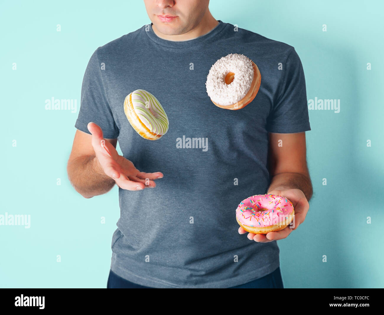 Jongleur Mann jongliert Donuts auf blauem Hintergrund. Donuts Lieferung oder ungesunde Ernährung Konzept. Flying glasierte Krapfen mit Streuseln und Kokosraspeln in männlichen Händen Stockfoto