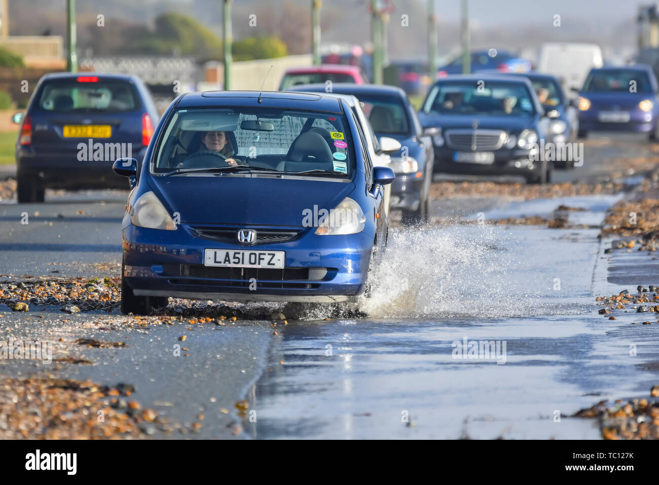 Autos fahren durch Pfützen und Strand Kies auf der Küstenstraße nach starkem Regen und stürmischem Wetter nach einem Sturm in West Sussex, England, UK. Stockfoto