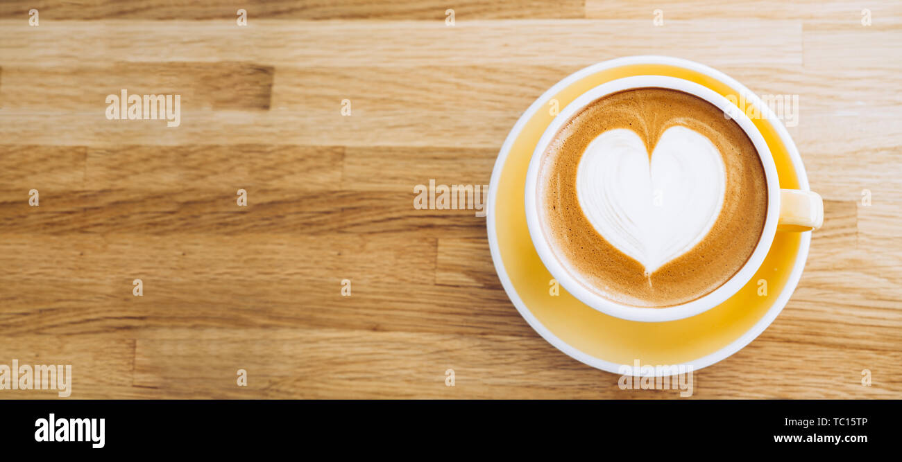 Blick von oben auf die heißen Cappuccino Tasse auf Holz- Fach mit Herz latte Kunst auf Holz Tisch im Cafe, Banner Größe Essen und Trinken Konzept. Kopieren Sie Raum, fo Stockfoto