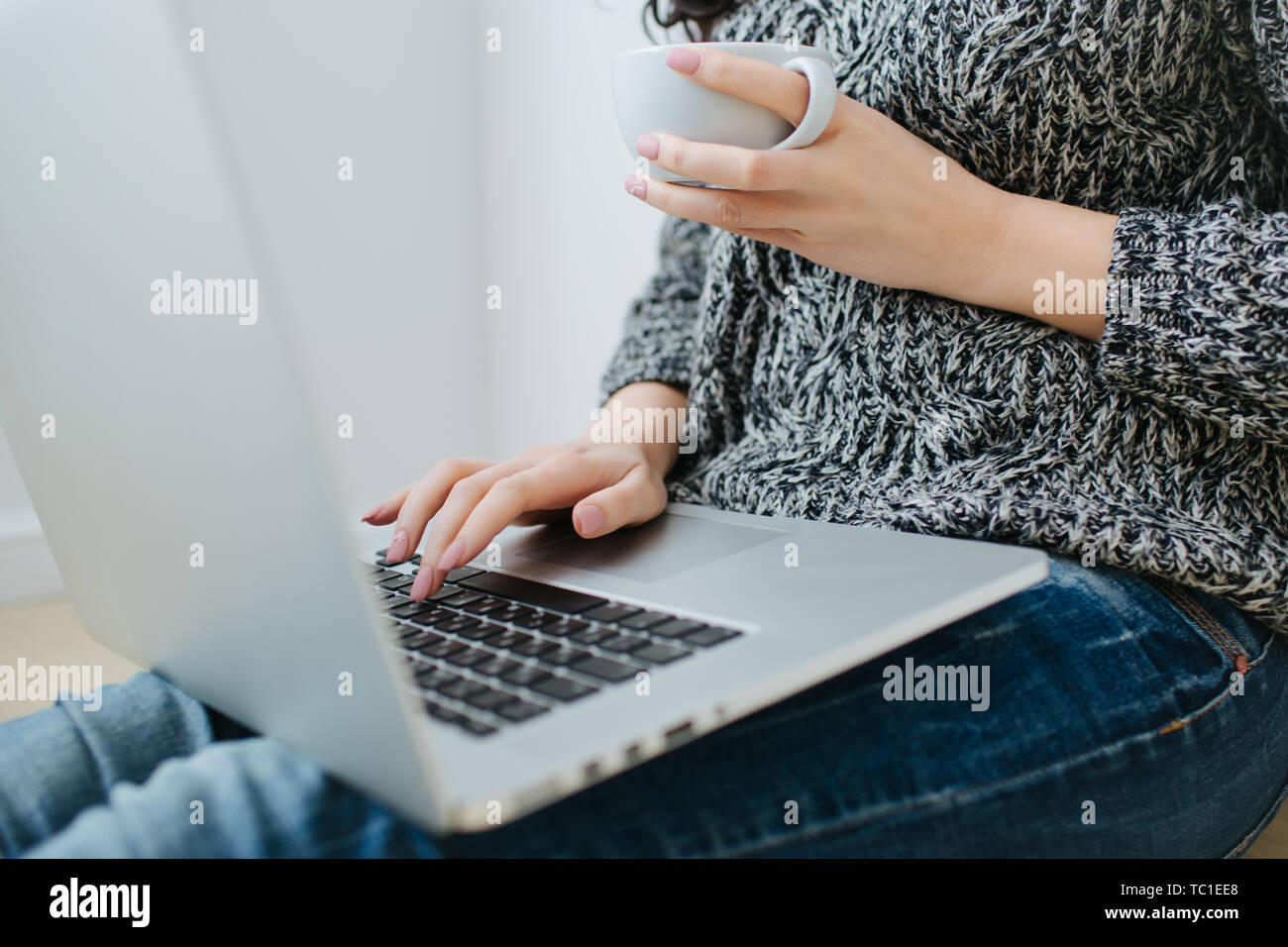 Arbeitsbereich mit Girl's Hand auf Laptop Tastatur und eine Tasse heißen Kaffee in weisser Tasse. Freelancer arbeiten. Arbeiten und Studieren von zu Hause aus Konzept. Stockfoto