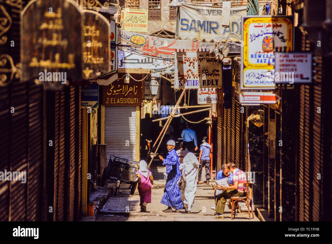 Luxor, Ägypten. Eine Straße Szene mit Banner Werbung Ladenbesitzer und zwei Touristen außerhalb ein Café die Zeitung lesen oder Karte. Foto: © Simon Grosset. Stockfoto