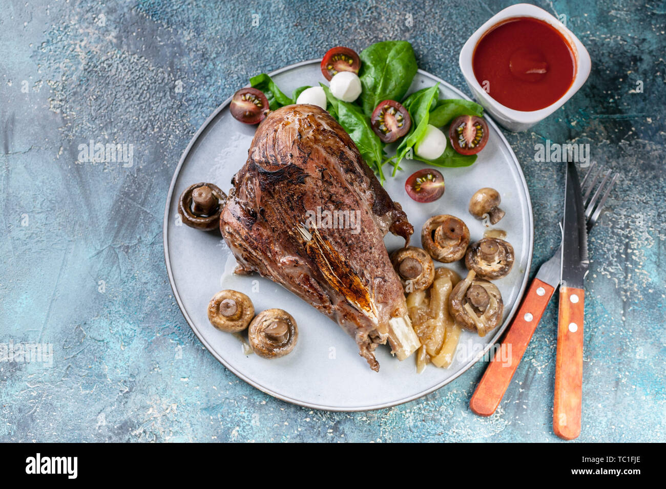 Gebackene Lamm mit Pilzen und Gewürzen und Kräutern auf einer runden Platte auf einen konkreten Hintergrund. Halal Fleisch und Lebensmittel. Ansicht von oben Stockfoto