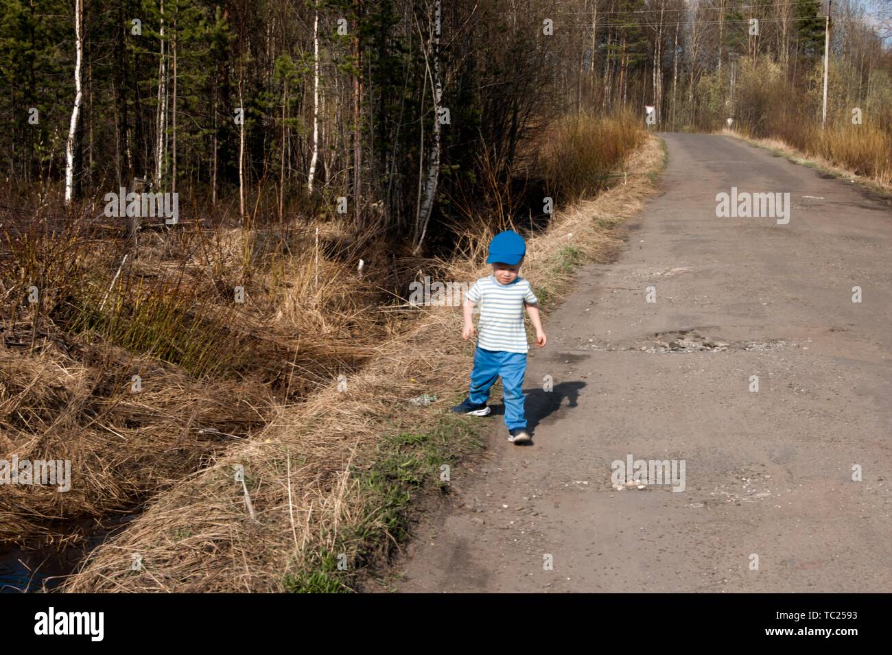 Der frühe Frühling, ein kleiner Junge von drei Jahren in blauen Hosen, eine auf einer Landstraße. Stockfoto