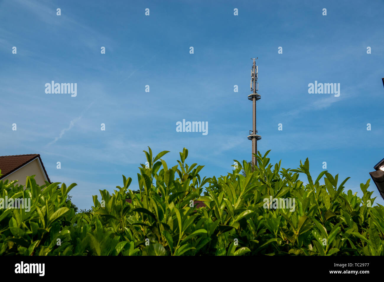 Ein radio Mast für das Mobilfunknetz überragt ein Wohngebäude in den blauen Himmel in einem Wohngebiet. Stockfoto