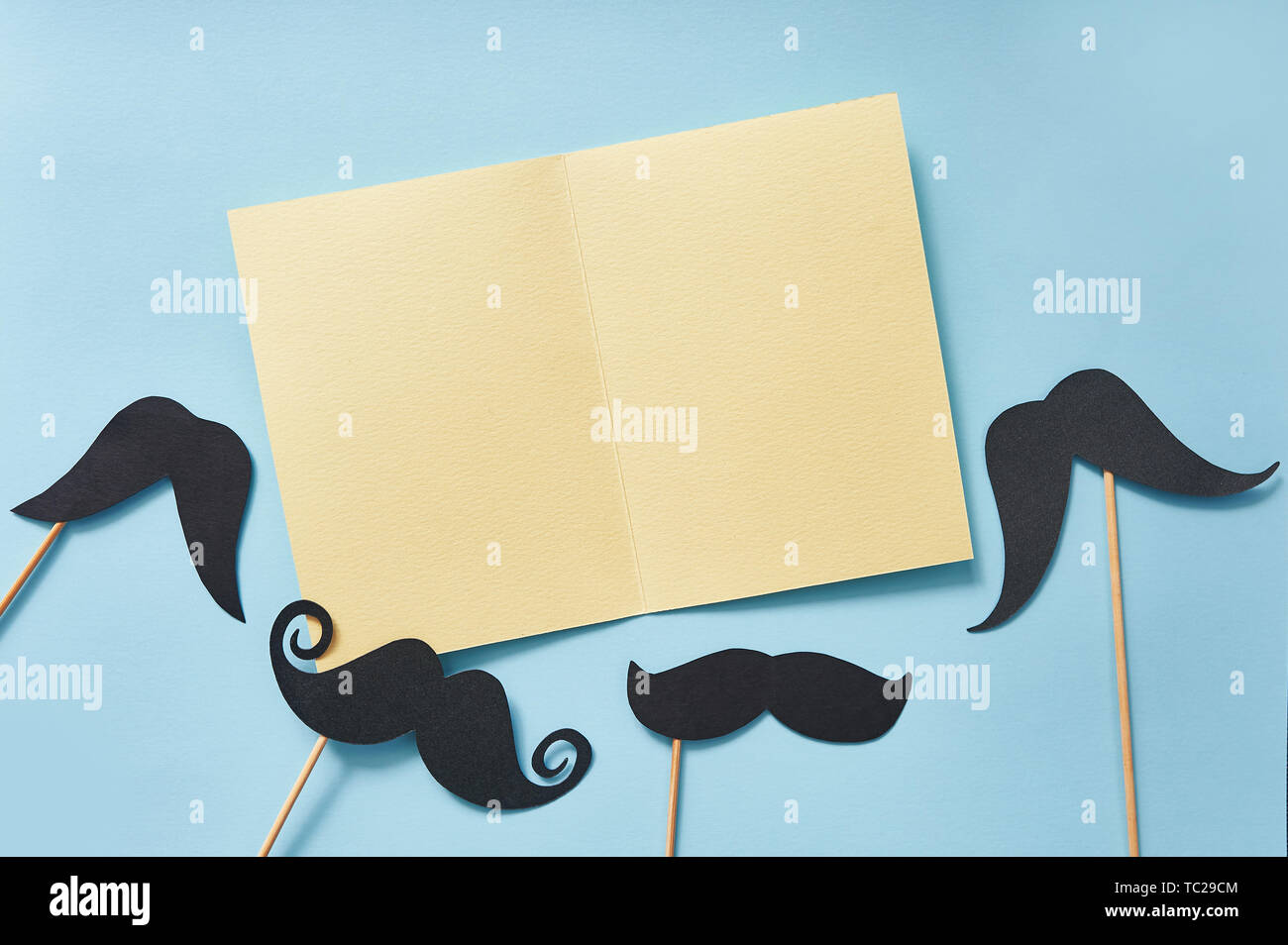 Mockup schwarzen Schnurrbärte auf blauem Papier Hintergrund Draufsicht. Glückwünsche zum Vatertag Grußkarte mit gelbem Blatt Papier und Platz für Text. Hipster Stockfoto