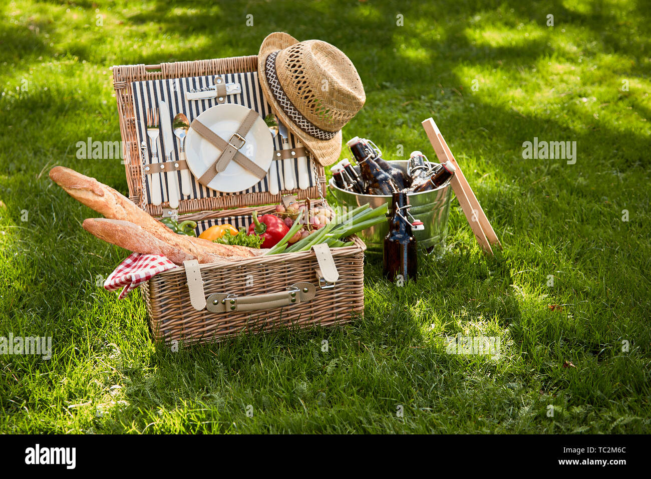 Vintage Style Sommer vegetarischen Picknick in einem Weidenkorb mit alten Strohhut und Kühler von Bierflaschen an der Seite auf saftig grünen Gras im Freien Stockfoto