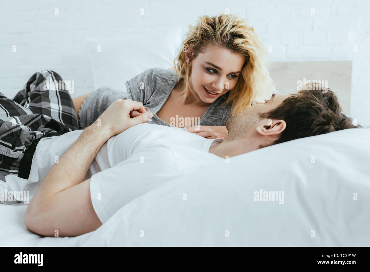 Fröhliche blonde Frau an Freund liegend auf Bett suchen Stockfoto