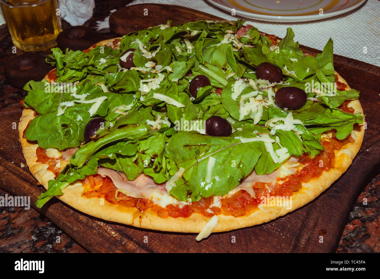 Lecker lecker Pizza mit Käse, Tomaten, Rucola, Oliven, Basilikum auf hölzernen Tisch Stockfoto