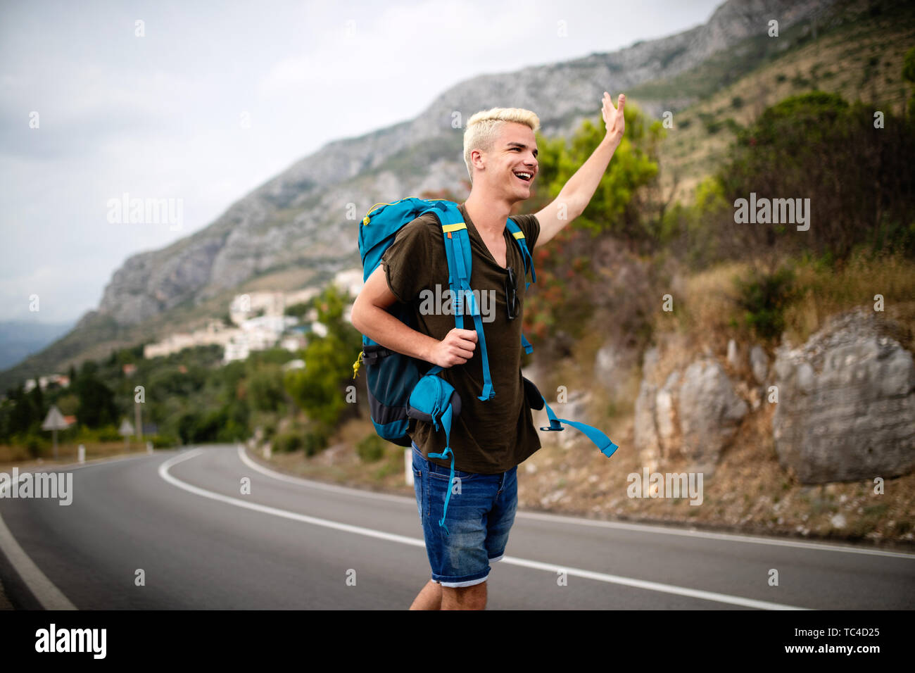 Per Anhalter, junge Reisende Mann versuchen Auto auf einer Forststraße zu fangen Stockfoto