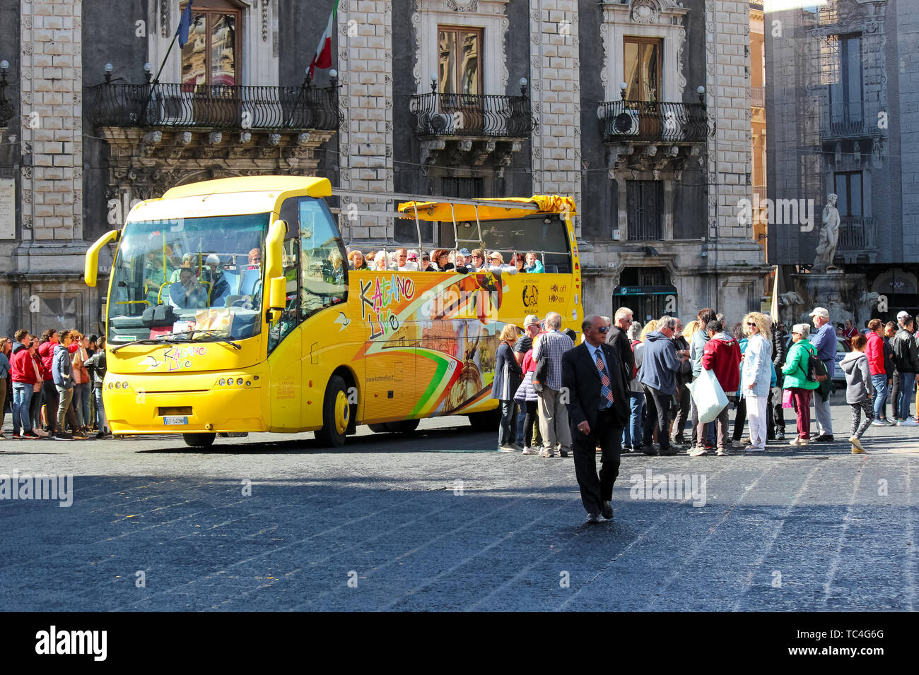 Catania, Sizilien, Italien - Apr 10 2019: Gelb Hop on Hop off Sightseeing Bus in Piazza Duomo mit einer Gruppe von Touristen. Der Hauptplatz im Zentrum der Stadt ist eine beliebte Touristenattraktion. Stockfoto