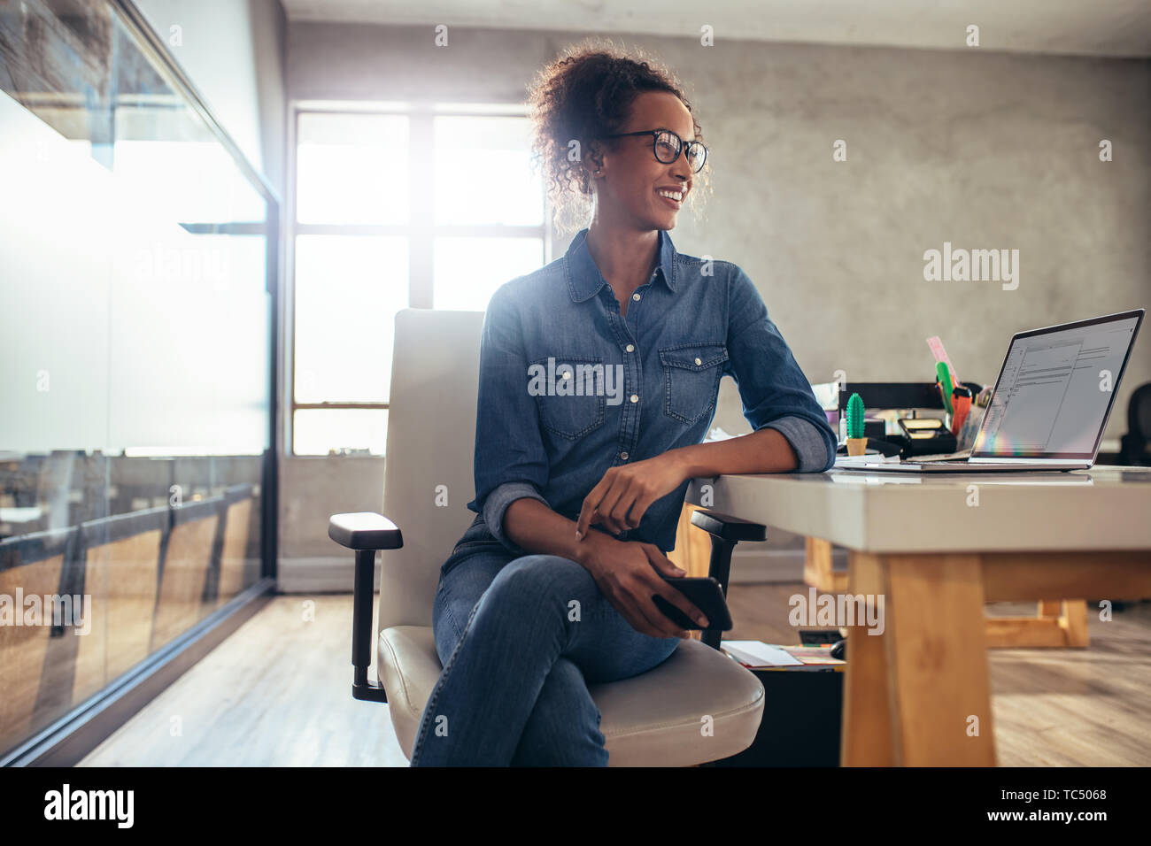 Junge Frau Unternehmer an ihrem Schreibtisch sitzen und Wegsehen. Geschäftsfrau, die an der Arbeit in einem kleinen Büro. Stockfoto