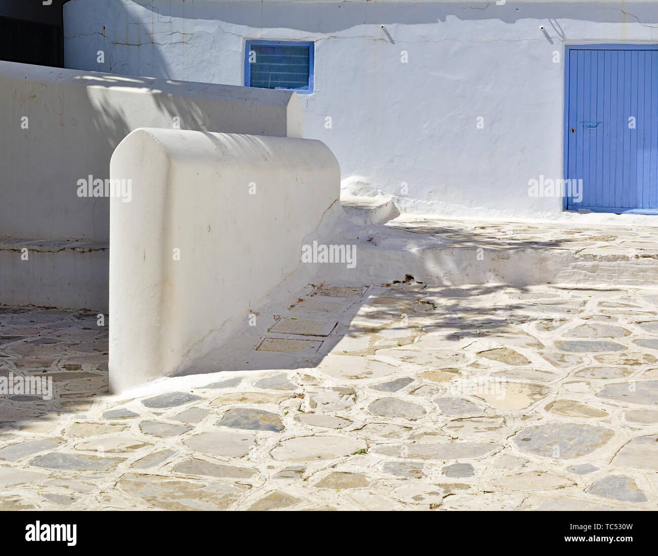 Weißes Haus mit blauen Fenstern und gepflasterten Hof, leeren Raum, Insel Tinos, Griechenland. Stockfoto