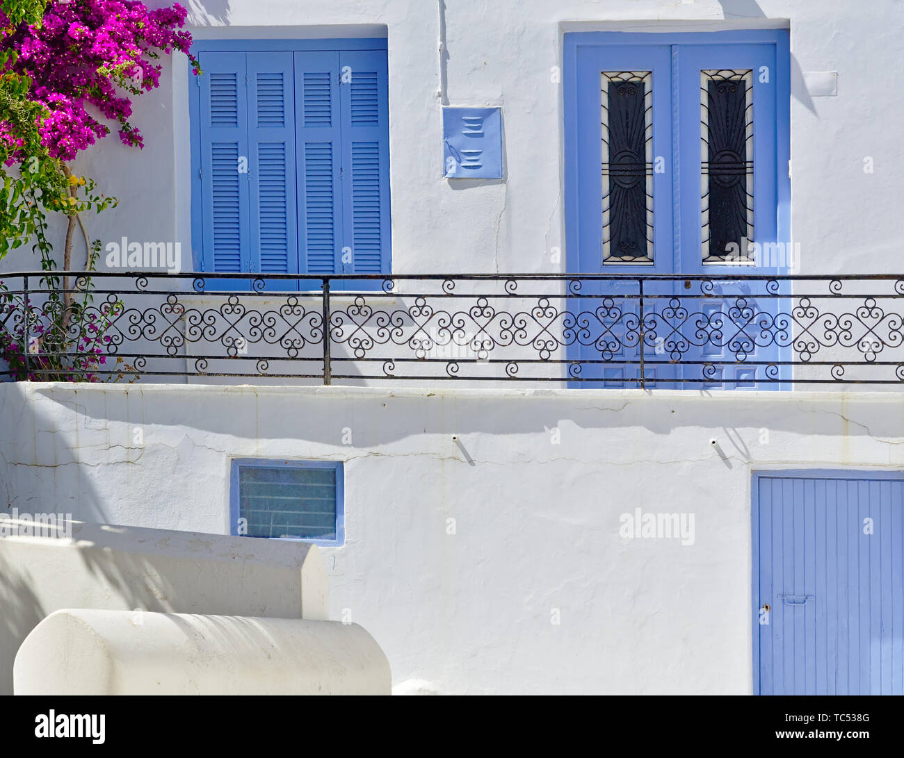 Schöne weiße Haus schließen sich ausführlich mit blauen Fenstern und Türen, lebendige Bougainvillea und Balkon mit Metall Geländer, Insel Tinos, Griechenland. Stockfoto