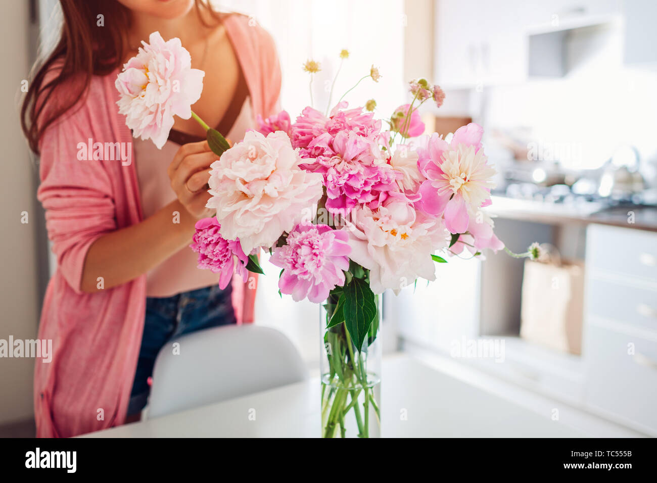 Frau setzt rosa Pfingstrosen Blumen in der Vase. Junge Hausfrau kümmert sich um Gemütlichkeit auf Küche. Komponieren Bouquet. Home Decor Stockfoto