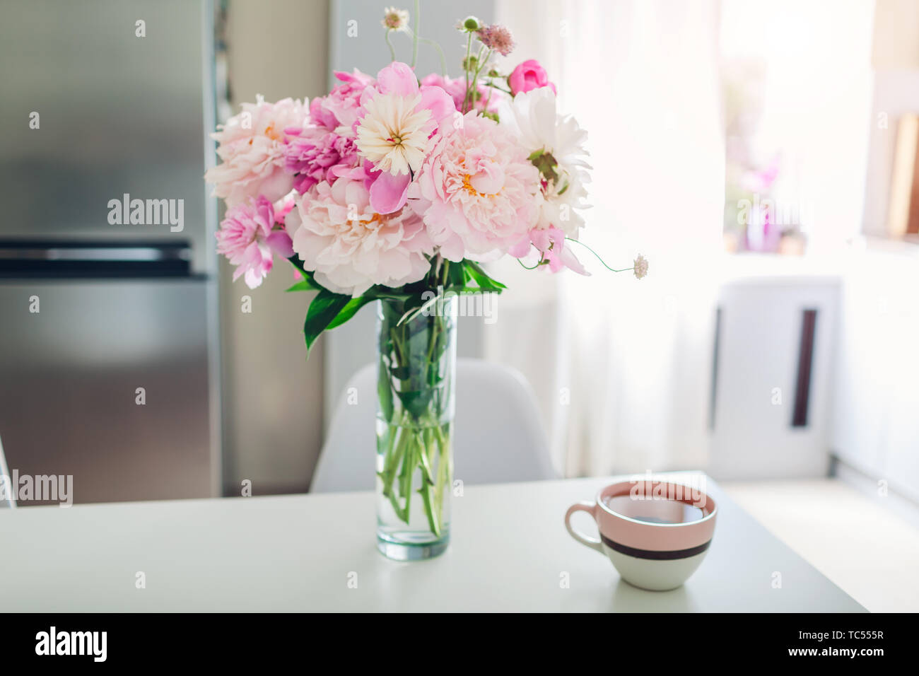 Rosa pfingstrosen mit Tee auf den Tisch. Moderne Küche Design. Innenraum weiss und silber Küche mit Strauß mit frischen Blumen geschmückt. Stockfoto