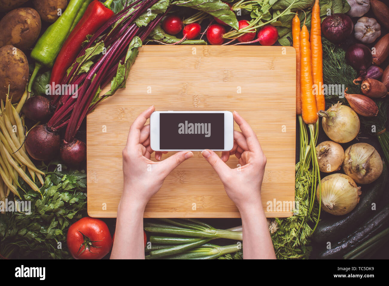 Hände mit Smartphone über Frisches Bio-Gemüse Hintergrund. Vegetarische Rezepte. Stockfoto
