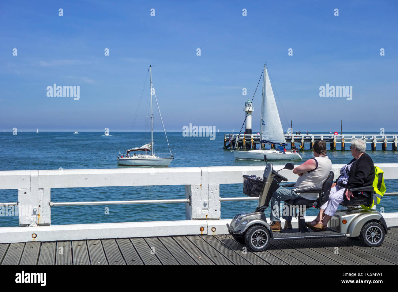 Behinderte Rentner in Duo zwei Person scooterverleih Segelboote beobachten auf See von Jetty im Seaside Resort im Sommer Stockfoto