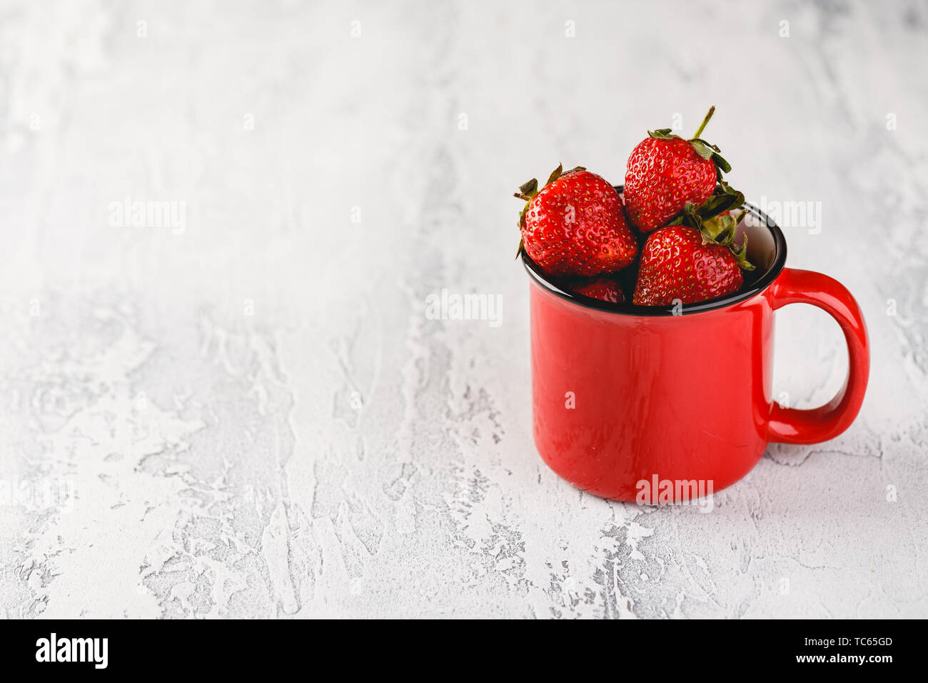 Frische Erdbeeren in rot Emaille Tasse auf grauem Hintergrund. Platz für Text. Stockfoto