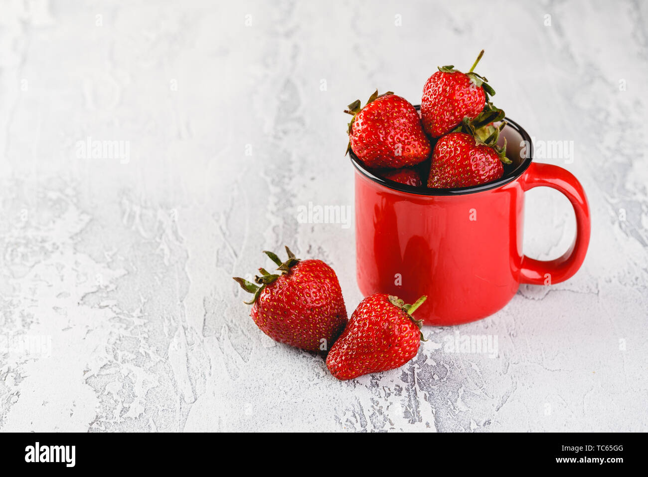 Frische Erdbeeren in rot Emaille Tasse auf grauem Hintergrund. Platz für Text. Stockfoto