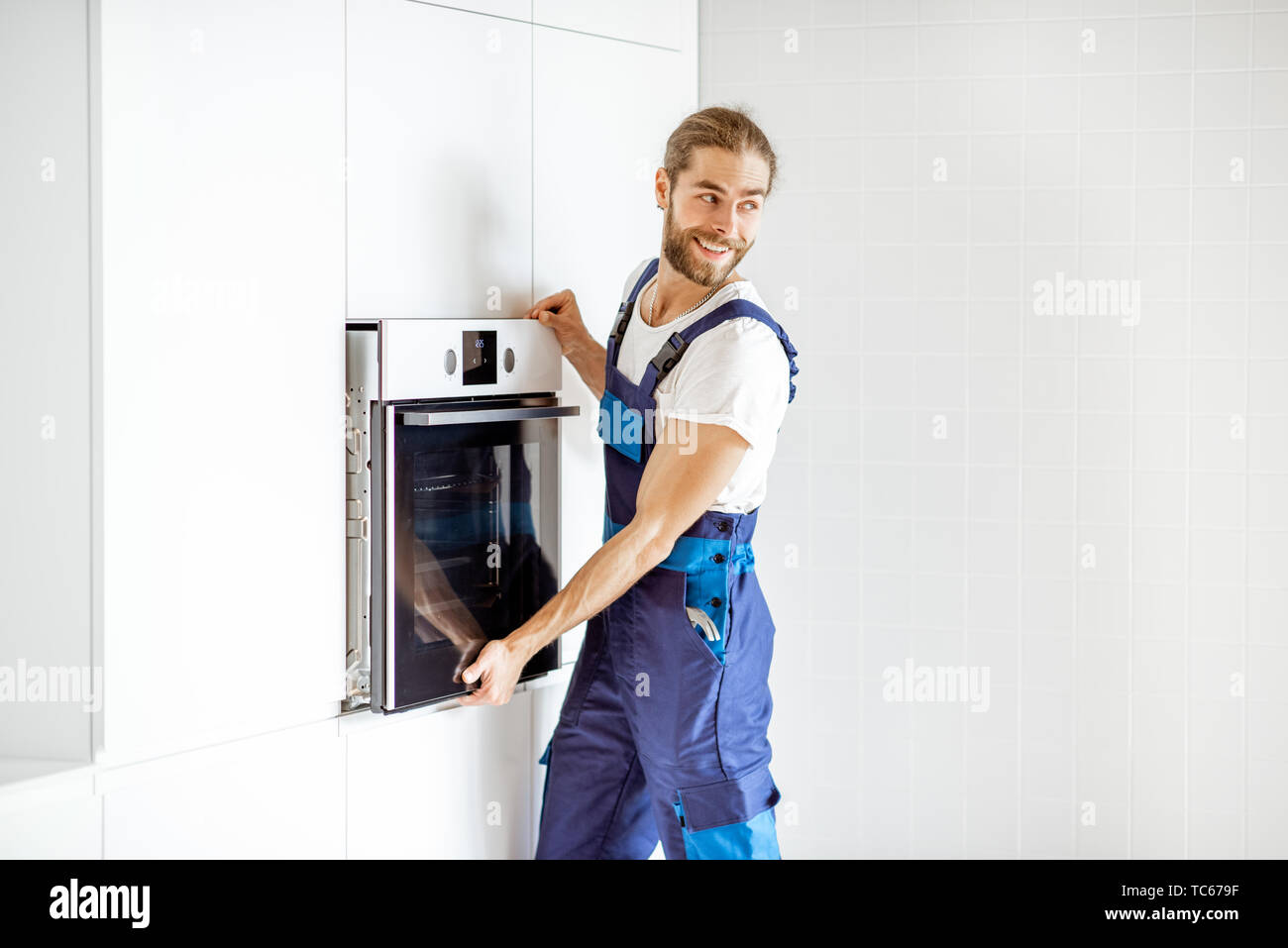 Stattliche workman in Arbeitskleidung Installation elektrischer Backofen in der Küche Regale in der modernen Küche zu Hause Stockfoto