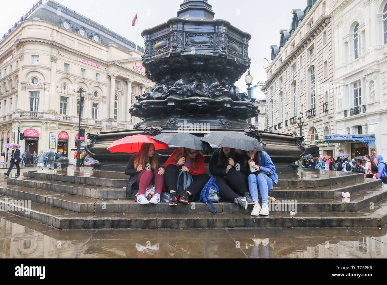 London, Großbritannien. 6. Juni, 2019. Die Menschen drängten sich unter Sonnenschirmen auf den Stufen des Eros Brunnen in Piccadilly Circus aus dem kurze Regenschauer Credit: Amer ghazzal/Alamy leben Nachrichten Stockfoto