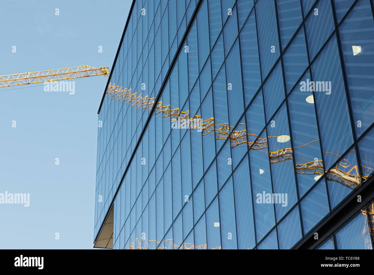 Ein Kran sitzt an der Basis von vielen modernen Gebäuden. Es gibt auch eine rote Cherry Picker. Die Gebäude sind Spiegel abgedeckt. Eine verblasste blauer Himmel mit niedrigen Clou Stockfoto