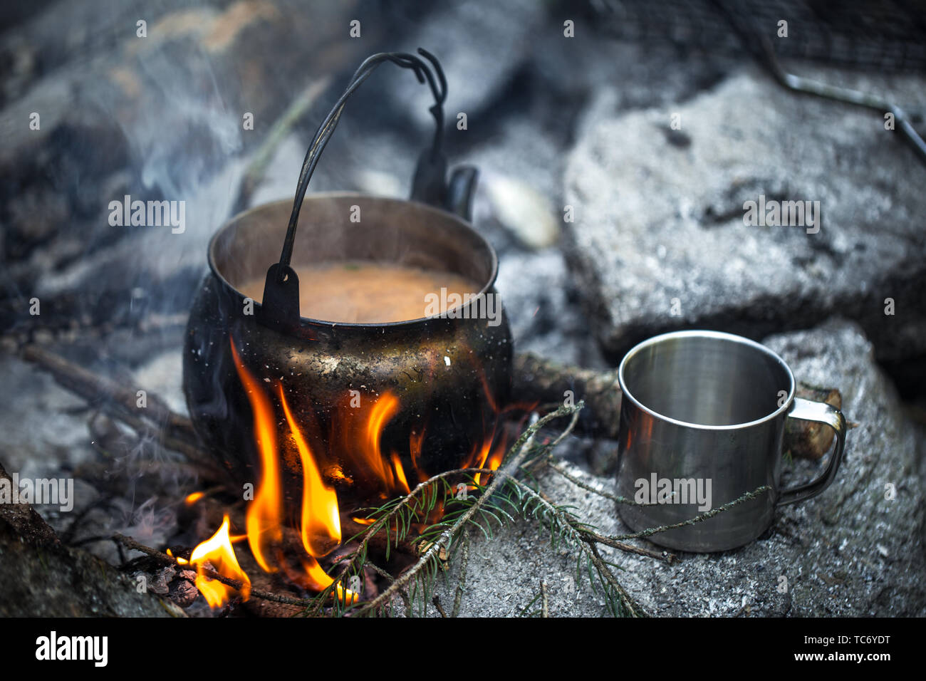 Kaffee mit Milch auf dem Scheiterhaufen gekocht. Ein Wasserkocher, ein Metall Becher, ein Feuer. Traveler's Frühstück Stockfoto