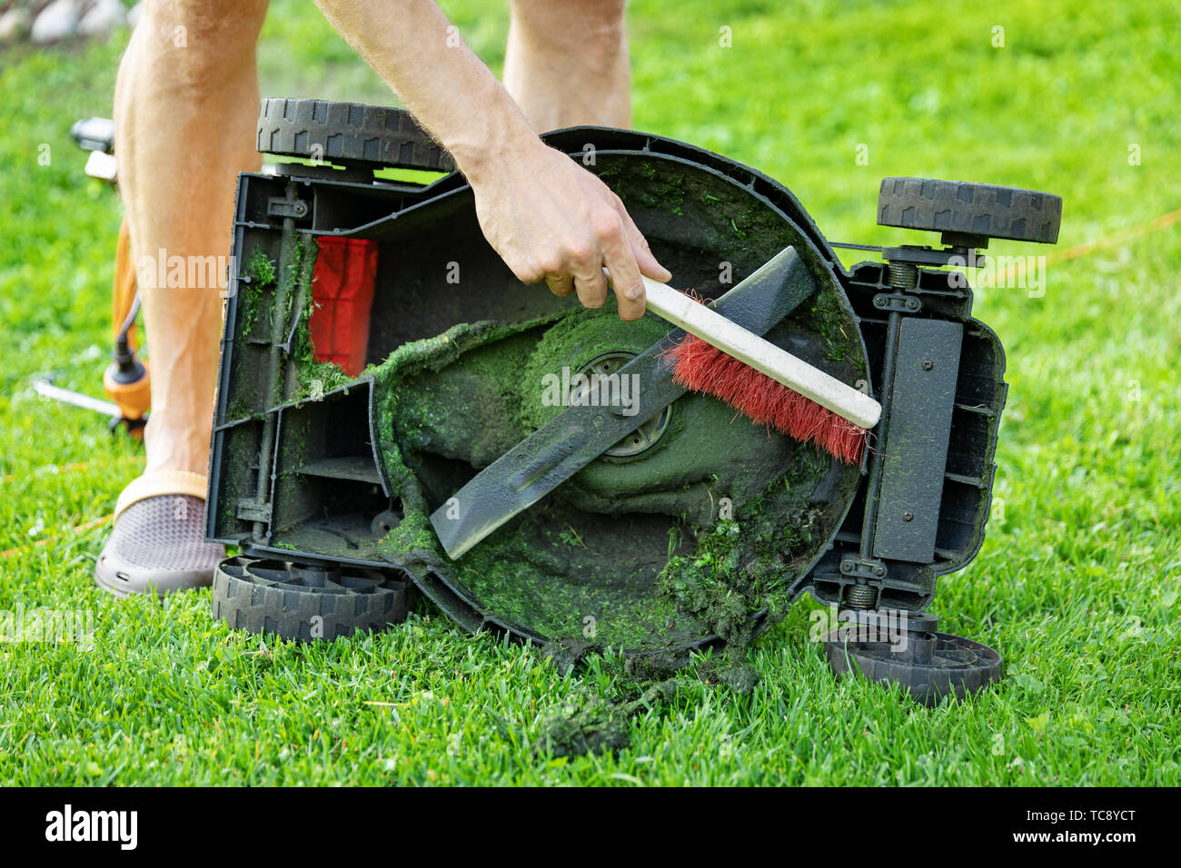 Mann mit Pinsel Reinigung Rasenmäher von Altes Gras Stockfoto