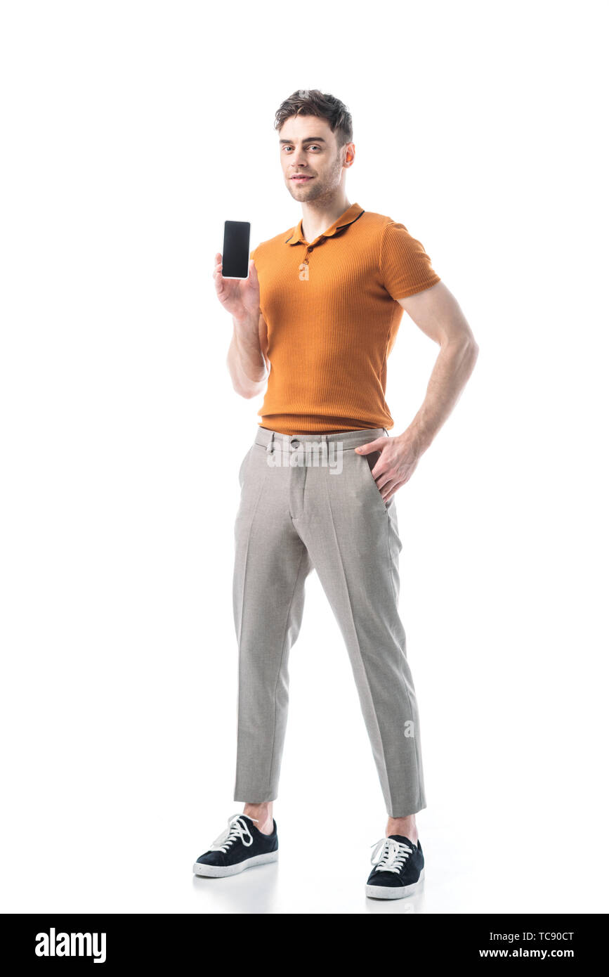 Gut aussehende Mann mit Hand in der Tasche halten Smartphone mit leerer Bildschirm isoliert auf weißem Stockfoto