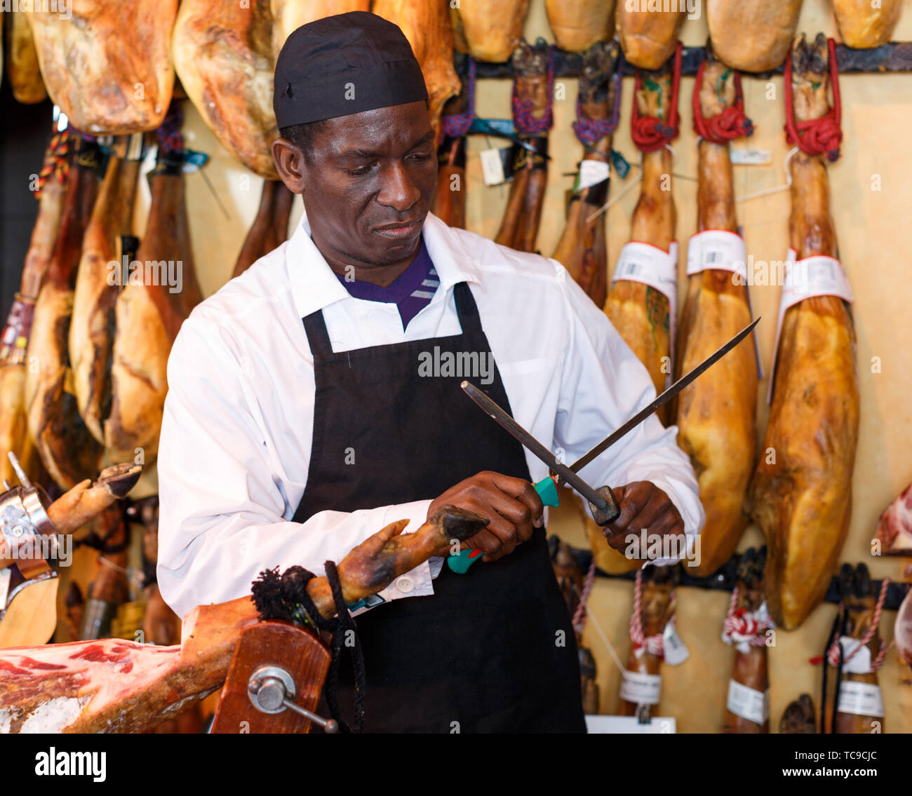 Zuversichtlich Afrikanische amerikanische Verkäufer Schärfen der Messer zum Schneiden von köstlichen Schinken in Metzgerei Stockfoto