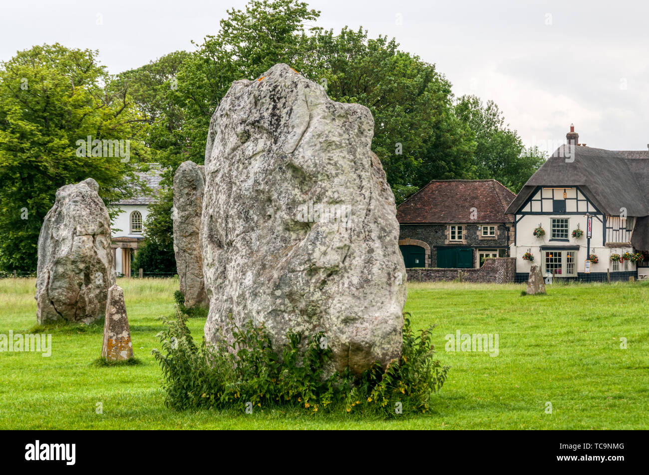 Steine der prähistorischen Steinkreis von Avebury mit dem Strohdach Village Pub, dem Red Lion, im Hintergrund. Stockfoto