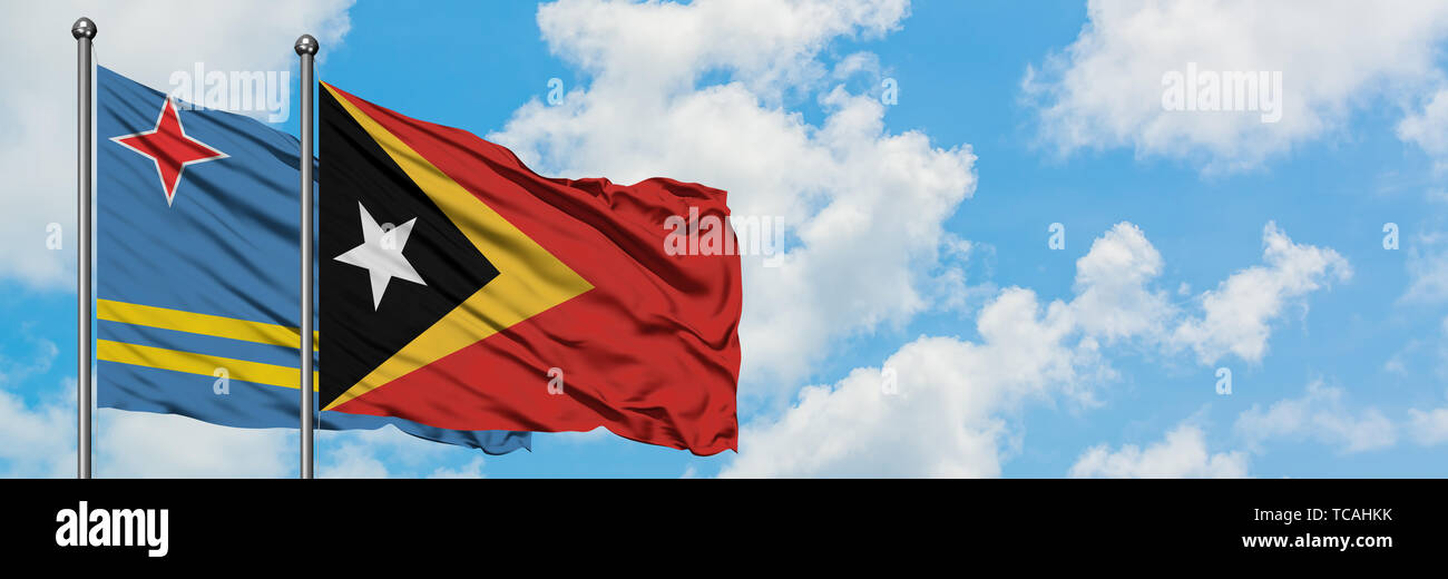 Aruba und Osttimor Flagge im Wind gegen Weiße bewölkt blauer Himmel zusammen. Diplomatie Konzept, internationale Beziehungen. Stockfoto