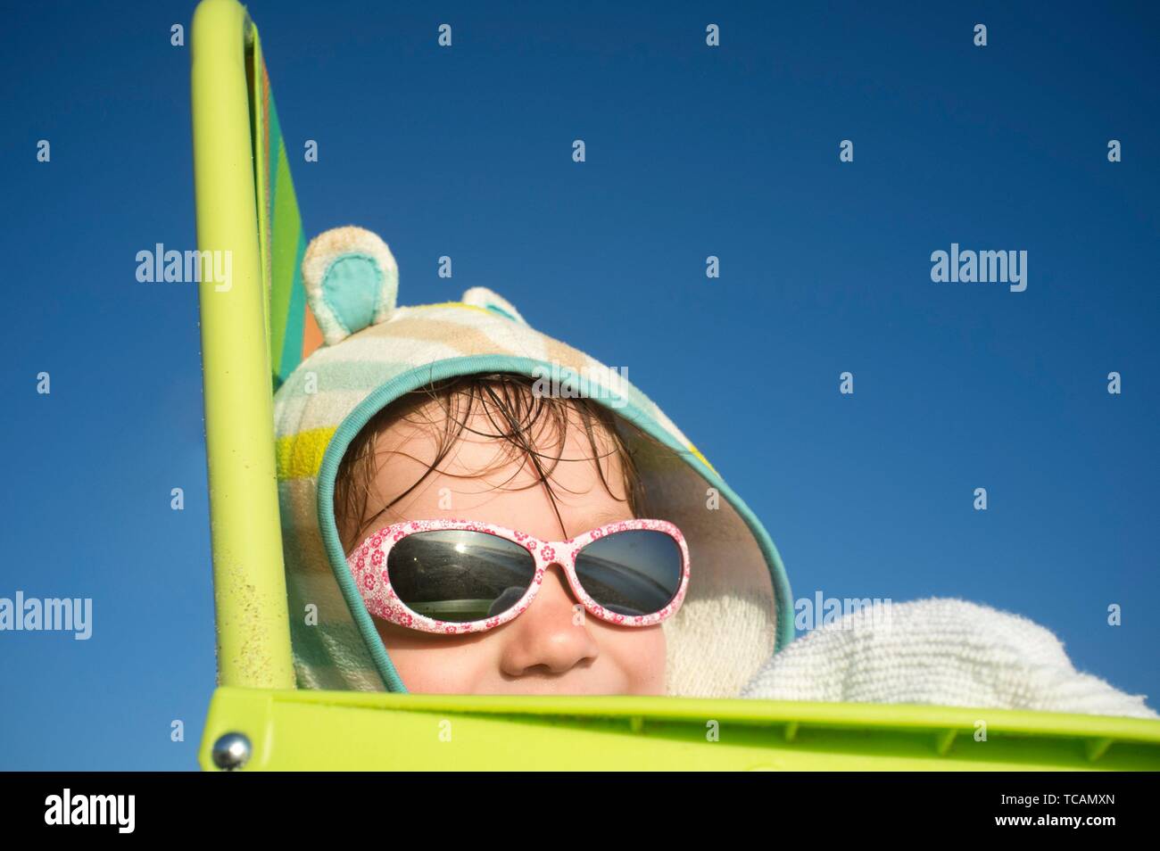 Lächelnd 3 Jahre baby boy über Strand Stuhl sitzen. Er trägt mit Kapuze poncho Handtuch und Sonnenbrille. Stockfoto