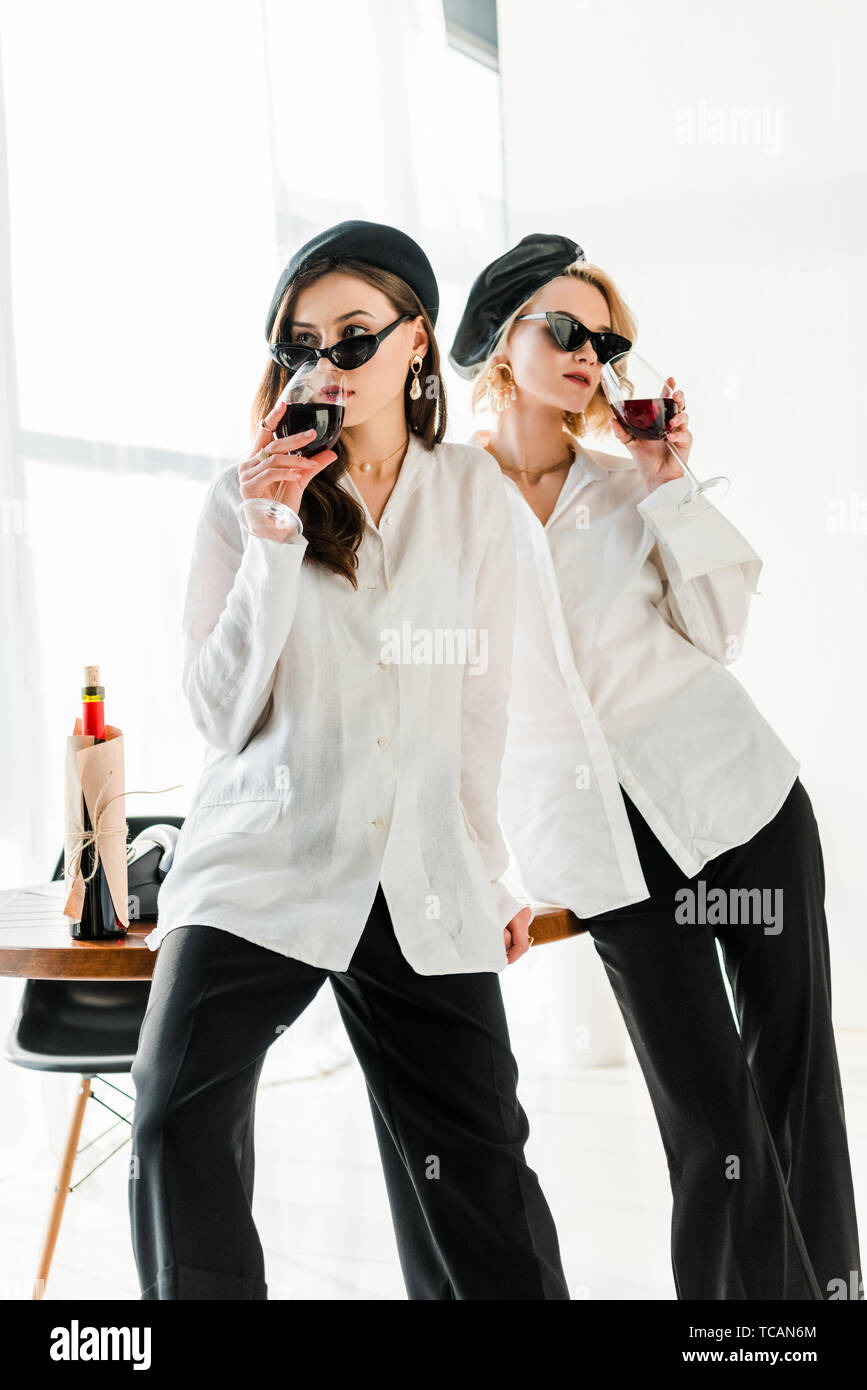 Elegante brunette und blond Freunde in schwarze Barette und Sonnenbrille trinken Rotwein Stockfoto