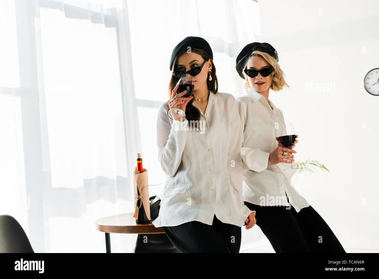 Elegante brunette und blonde Frauen in schwarze Barette und Sonnenbrille trinken Rotwein Stockfoto