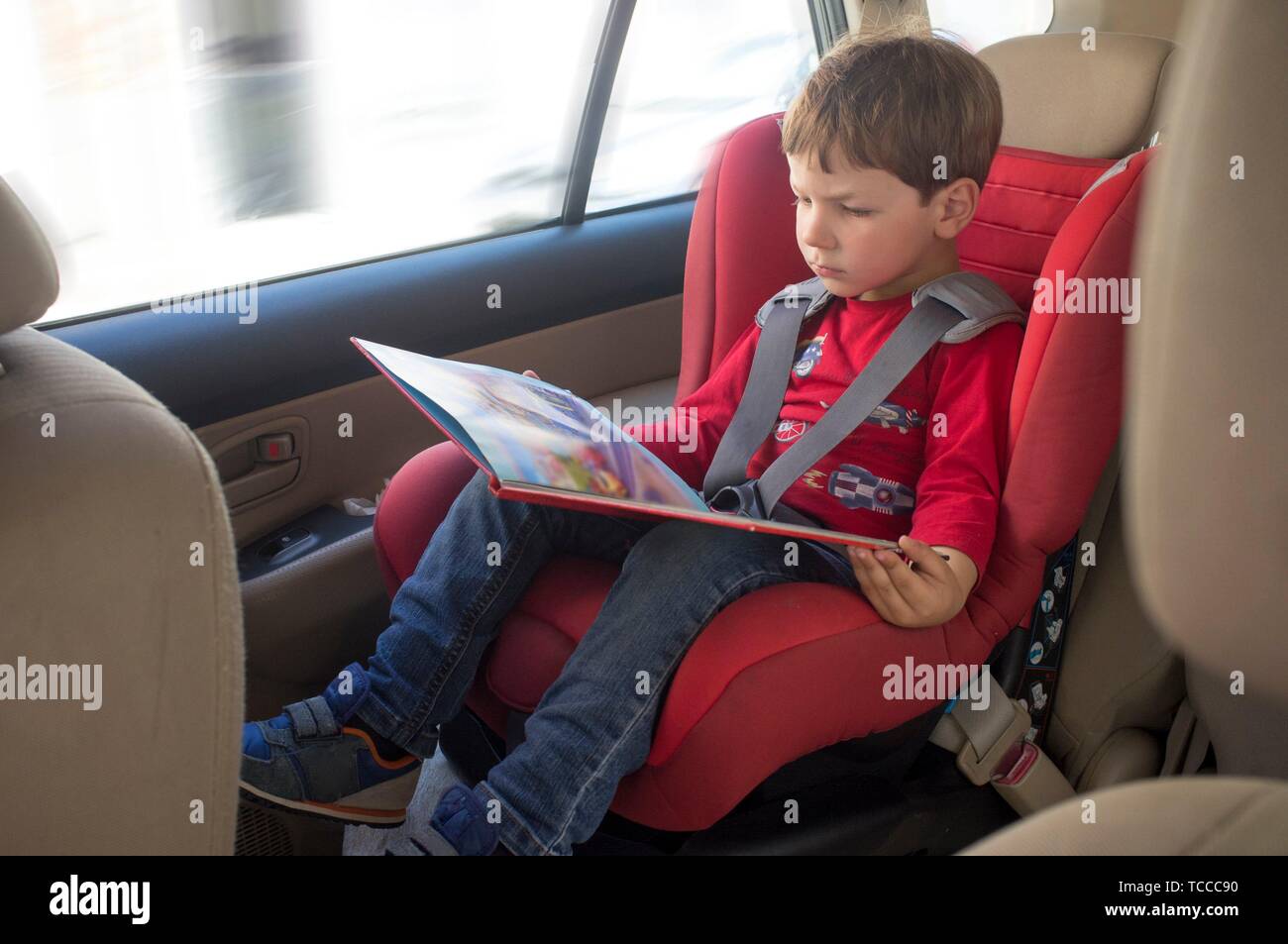 Toddler boy Lesung buchen Sie im Kindersitz. Unterhaltung im Auto für Kinder Konzept. Stockfoto