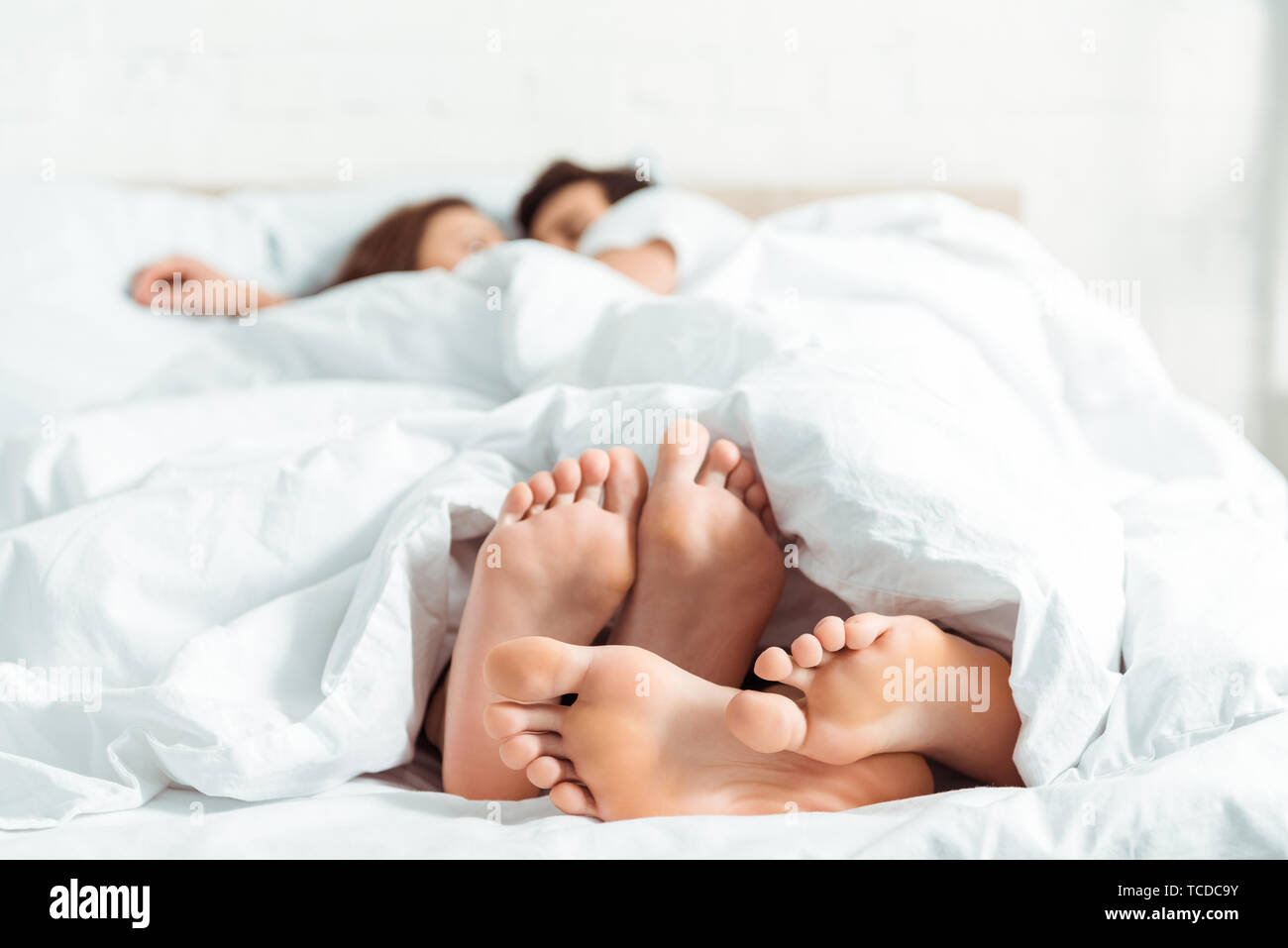 Selektiver Fokus der Barefoot der jungen Frau und Mann unter der Decke im Bett lag, Stockfoto