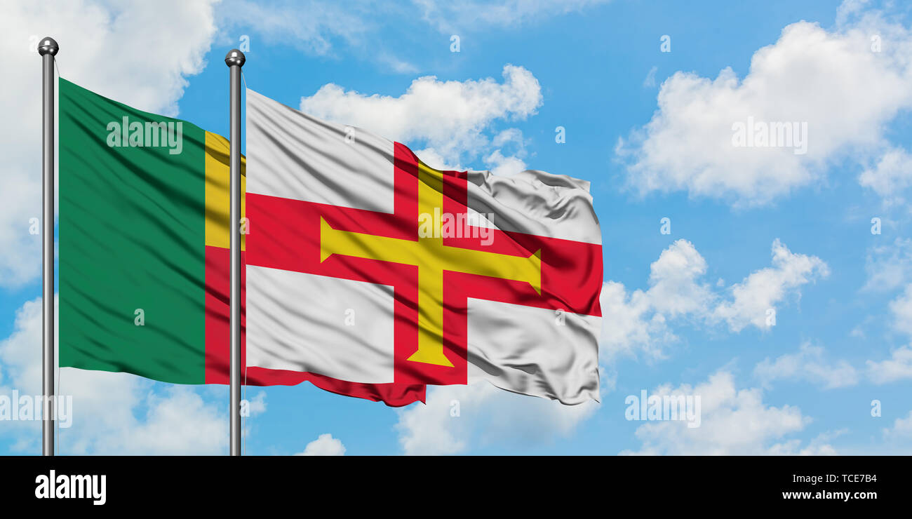 Benin und Guernsey Flagge im Wind gegen Weiße bewölkt blauer Himmel zusammen. Diplomatie Konzept, internationale Beziehungen. Stockfoto