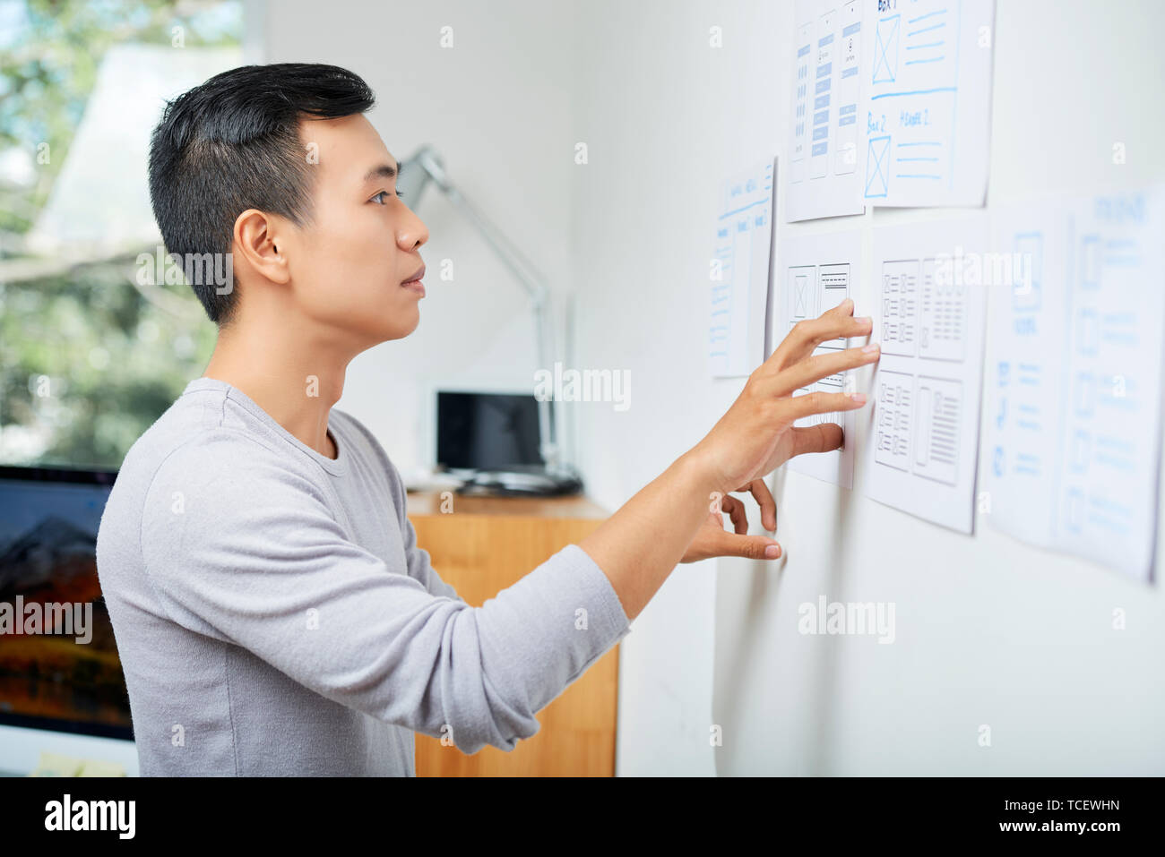 Nachdenklich jungen asiatischen UX-Designer bei Dokumenten mit Drahtmodellen hängen an der Wand im Büro suchen Stockfoto