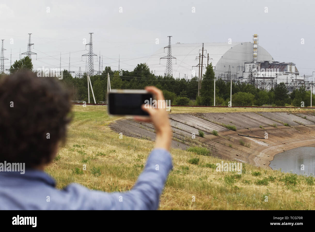 Pripyat, Ukraine. 7. Juni 2019. Ein Besucher nimmt Fotos der neuen Schutzkonstruktion in der 4. Block des Kernkraftwerks Tschernobyl in der Sperrzone von Tschernobyl in Pripyat. Der HBO-TV-Miniserie Tschernobyl, in den USA und in England im Mai 2019 uraufgeführt, schildert die Zeit nach der Katastrophe, einschließlich der Reinigung und die anschließende Untersuchung. Credit: ZUMA Press, Inc./Alamy leben Nachrichten Stockfoto