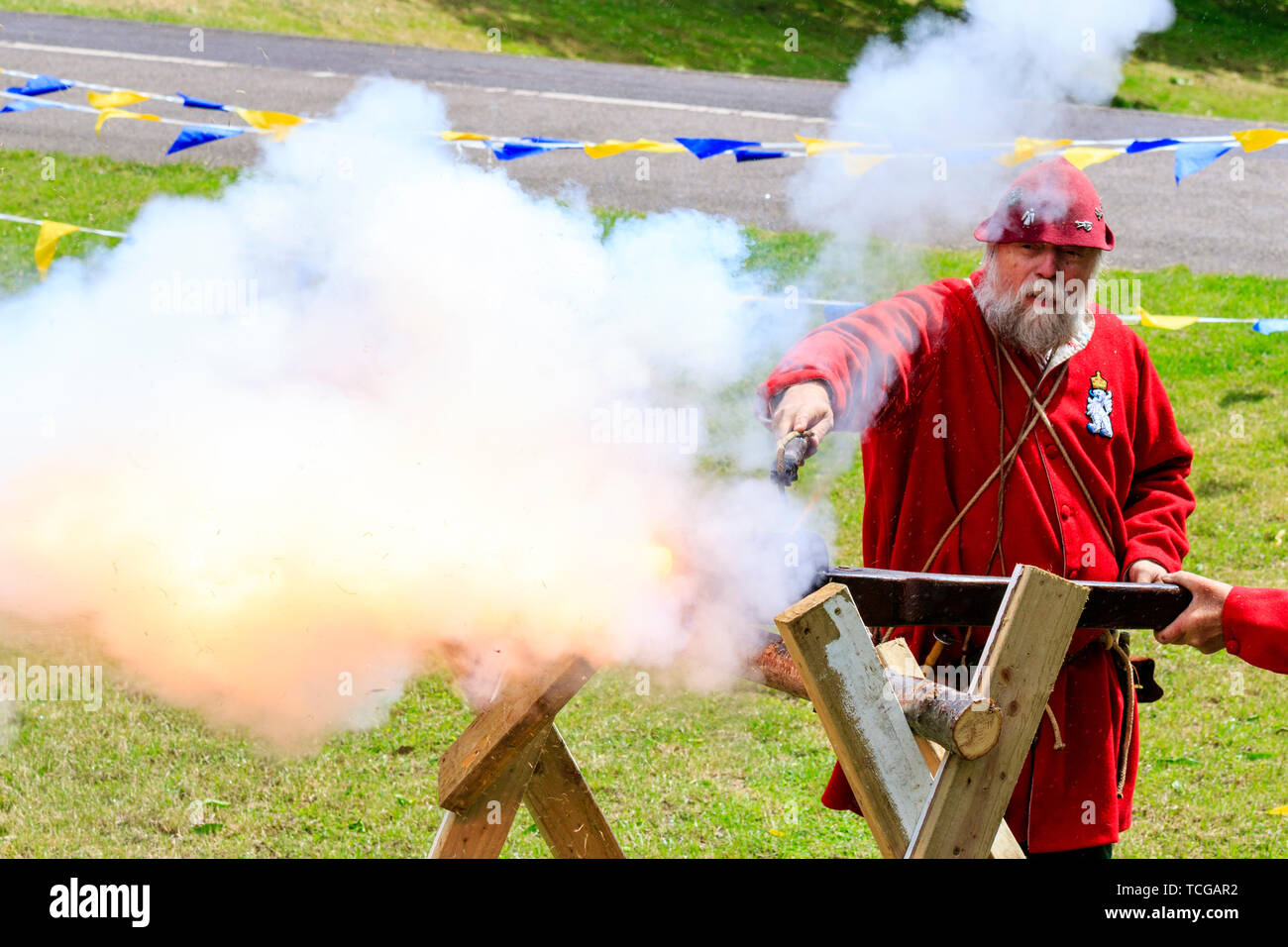 Le mittelalterliche Wochenende Re-enactment Veranstaltung am Sandwich Stadt in England. Mann gekleidet in mittelalterlichen Roten gunner Outfit und feuerte eine hand Cannon an einer Halterung montiert. Rauch und Feuer. Stockfoto