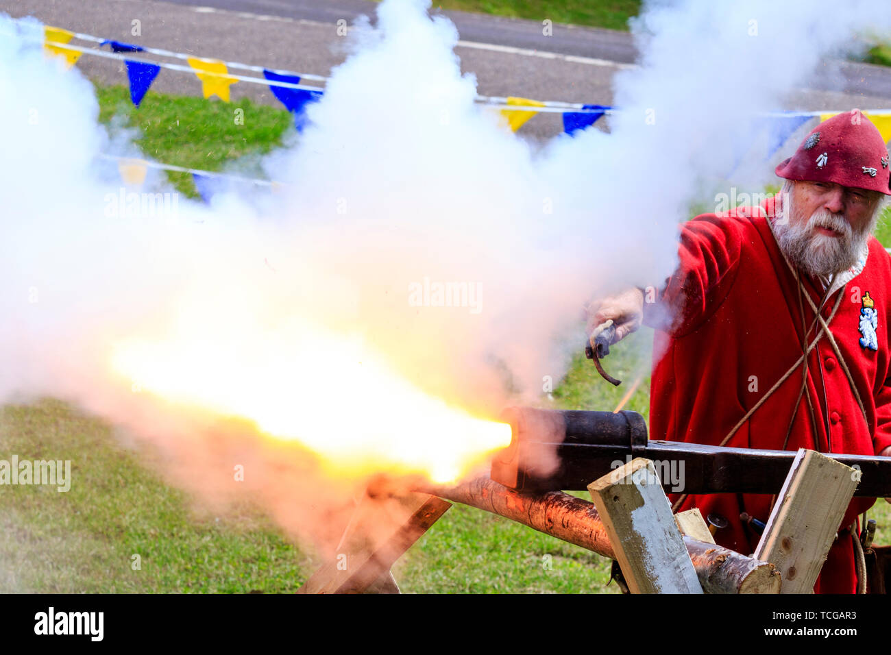 Le mittelalterliche Wochenende Re-enactment Veranstaltung am Sandwich Stadt in England. Mann gekleidet in mittelalterlichen Roten gunner Outfit und feuerte eine hand Cannon an einer Halterung montiert. Rauch und Feuer. Stockfoto